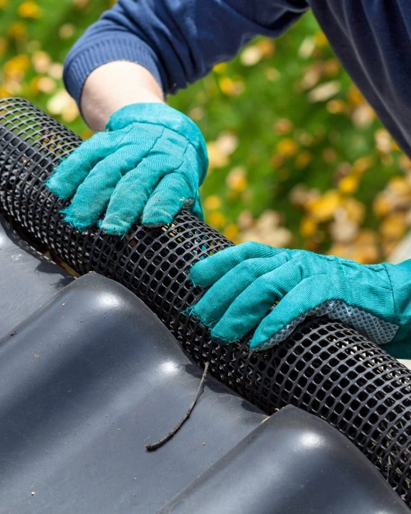 Gloved hands working beside a gutter guard